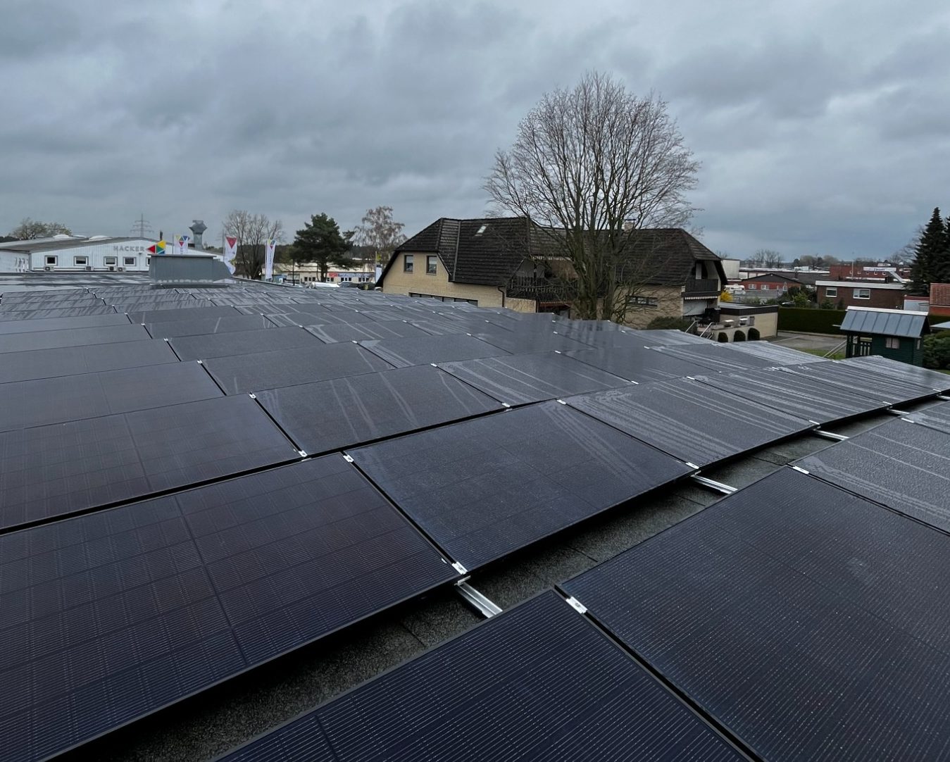 Sun Earth Photovoltaik-Module 435Watt full Black Dach mit Solarpaneelen, grauer Himmel und Wohngebäude im Hintergrund.